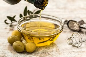 Olive oil being pours into a container, with fresh olives next to it.