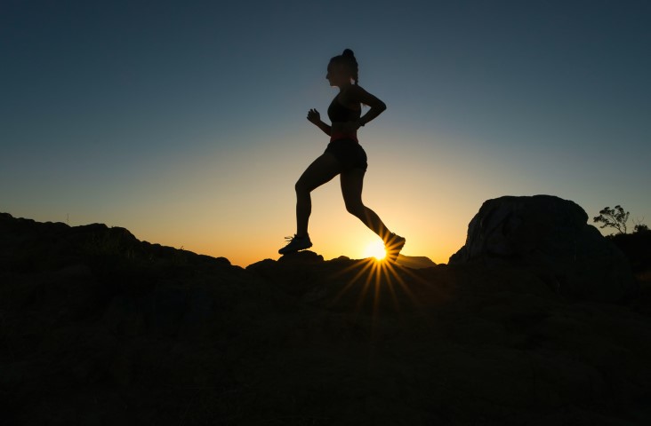 Silhouette of someone running with the run in the background