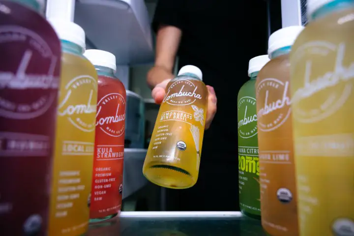 Someone grabbing a bottle of kombucha from a fridge, with other bottles of kombucha next to it.