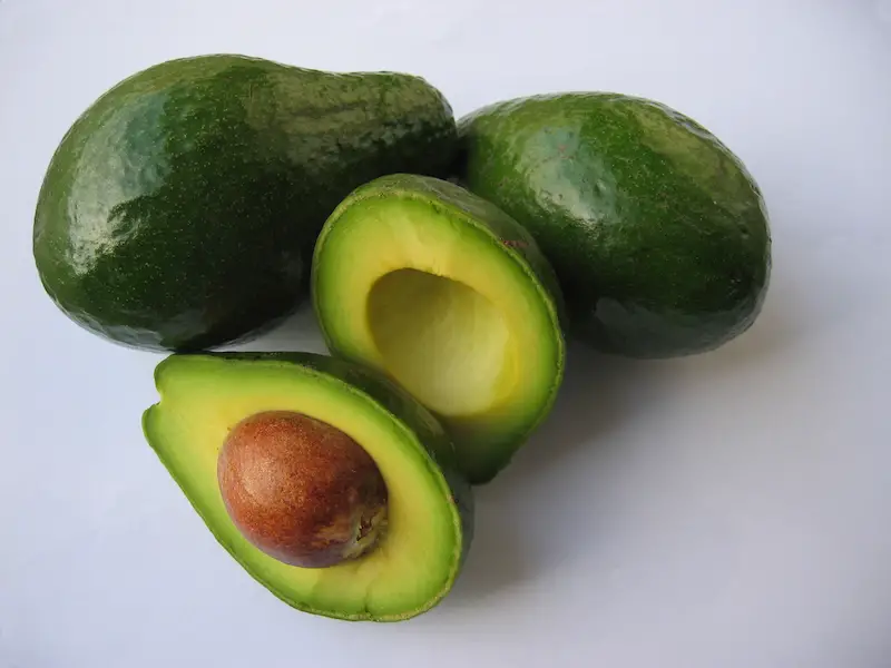 3 Avocados, of which one is cut in half exposing the seed.